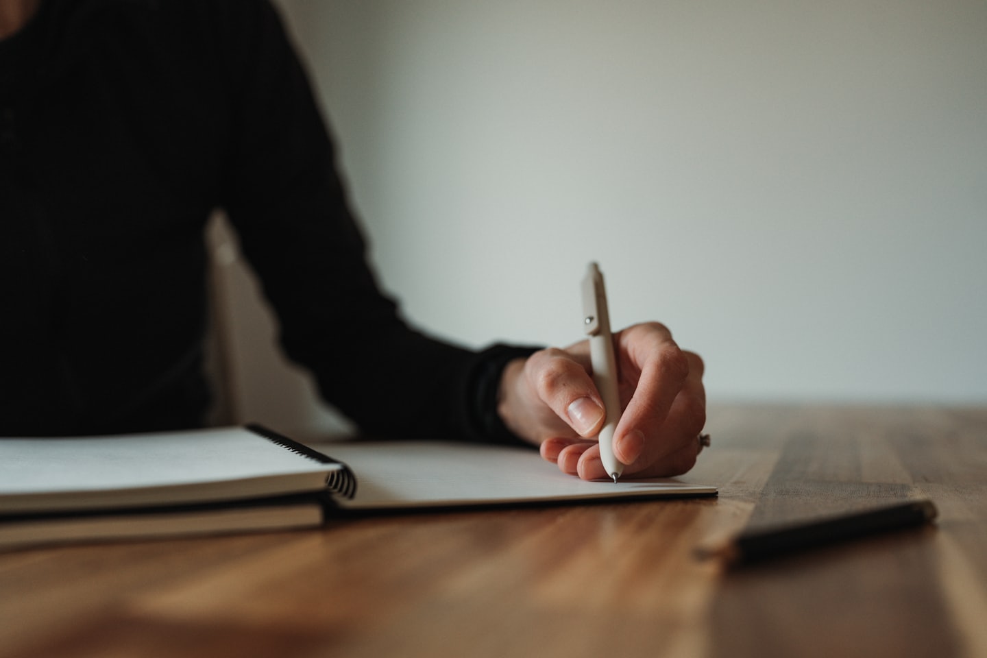 A person writes with a beige pen in a spiral notebook.