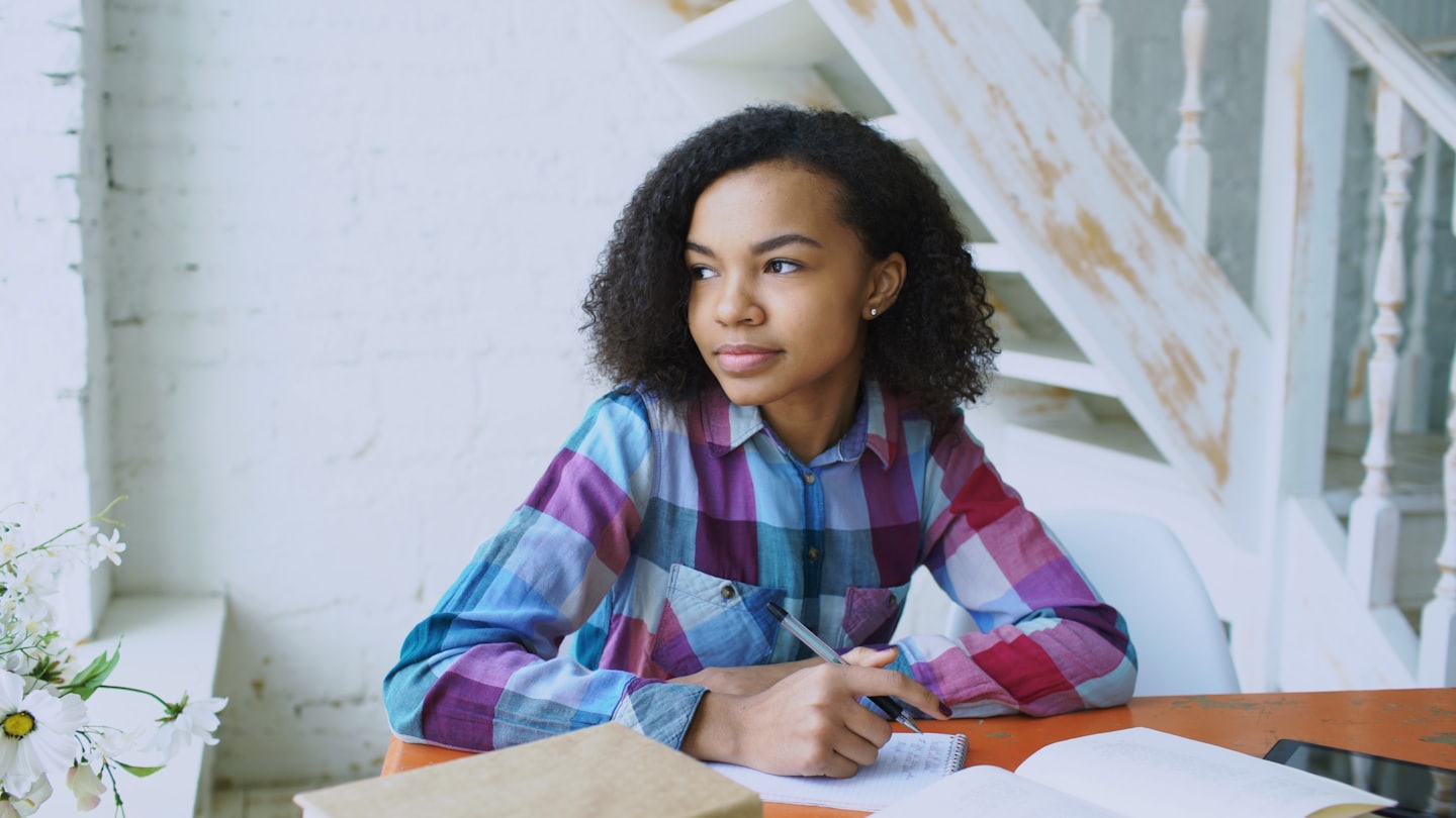 Woman taking notes at an orange table next to books.