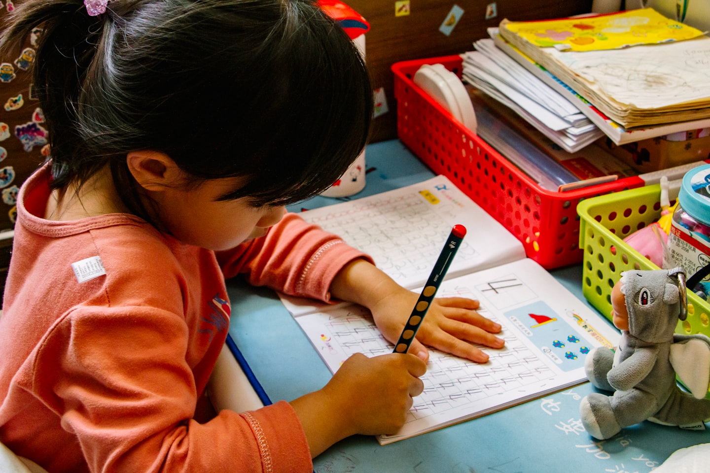 Child practicing writing in a workbook at a busy desk.