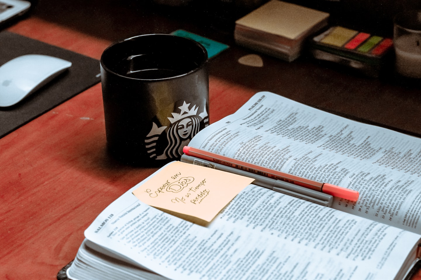 Open Bible with pens and coffee on a wooden desk.