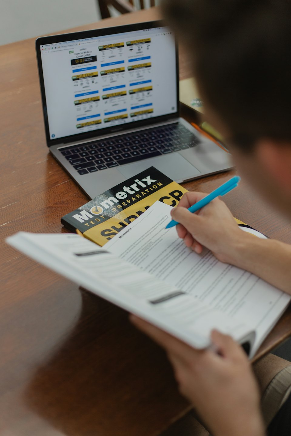 Student writing in a textbook at a desk with a laptop.